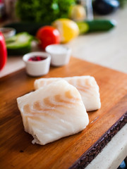 Fresh raw cod with herbs served on cutting board on wooden table