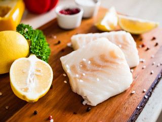 Fresh raw cod with herbs served on cutting board on wooden table