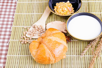 croissant baked bread with Milk in bowl, soy bean on spoon and  spices on wooden bamboo. copy space for text. top view