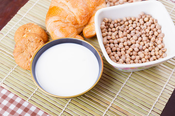 Milk in bowl with croissant baked bread, soy bean in cup on wooden bamboo and copy space for text. top view
