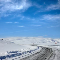 Fotobehang Empty frozen asphalt road and snow covered landscape with mountain over blue sky in winter time © jokerpro