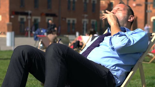 Businessman sleeping, waking up and lying on sunbed in the city