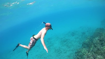 Snorkeling man swims up to the surface, removes mask and smiles at camera 4K