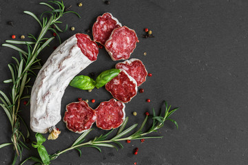 salami jerked sausage with rosemary and pepper over black slate background. top view with copy space