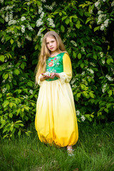 Blond young girl posing in a yellow green dress near birch trees