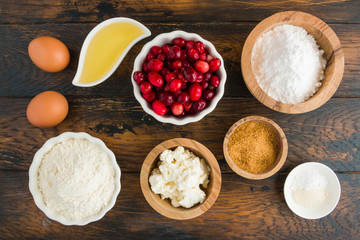 Ingredients for muffins. Flour, eggs, olive oil, cranberries, ricotta, brown and icing sugar, baking powder, vanilla. White bowls on wooden rustic table, top view