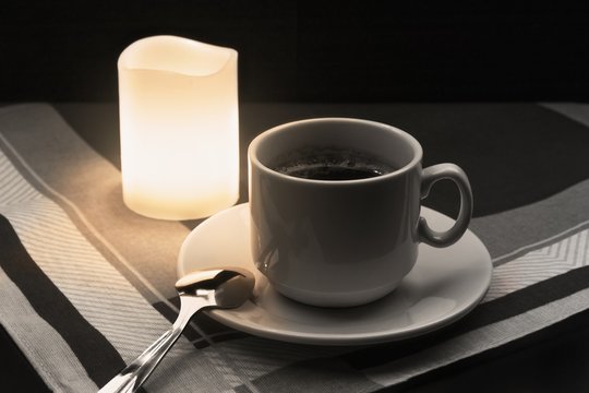 Cup of coffee with spoon and candle on fabric background