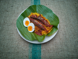 Selective focus one of malaysian favourite breakfast called Nasi Kuning, the yellow rice added with spicy fried fish and boiled egg. Served on banana leaf on the top of the rustic sacks.