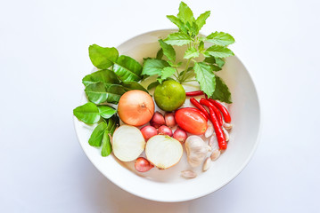 Herbal vegetables in a white bowl isolated on white background : gaffer lime leaves, holy basil leaves, lime, onions, shallots, garlics, red spicy chilies and tomato