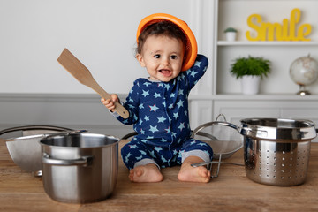 Happy baby playing drums with utensils on kitchen table