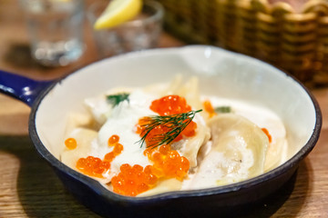 Dumplings  (pelmeni or vareniki) with sour cream and red salmon caviar lie on a frying pan.