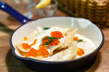 Dumplings  (pelmeni or vareniki) with sour cream and red salmon caviar lie on a frying pan.