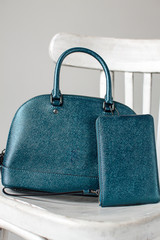 women leather bag and purse (dark green, blue, turquoise color) on a white wooden chair (close up)