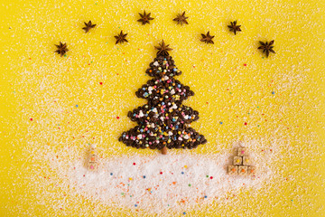 Christmas tree made from coffee beans and Christmas gifts made from waffles decorated coconut chips, anise star and multicolored culinary sprinkling on a yellow background, top view.