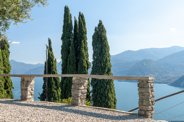 High cypresses close to a stone staircase leading to a mountain lake at sunny day - 233927769