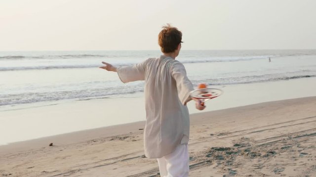 Senior woman practicing tai chi balloon ball on the beach at sunset