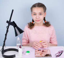 girl with two pigtails, sitting at the table and holding a container for storing contact lenses