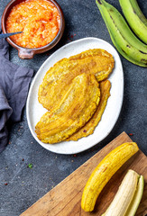 COLOMBIAN CARIBBEAN CENTRAL AMERICAN FOOD. Patacon or toston, fried and flattened whole green plantain banana on white plate with tomato sauce. Black background, top view