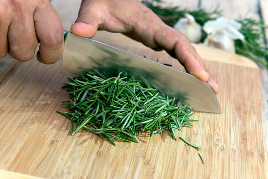 Chopping rosemary with knife on cutting board