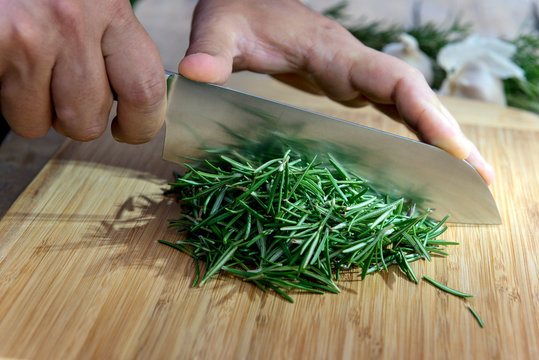 Chopping rosemary with knife on cutting board
