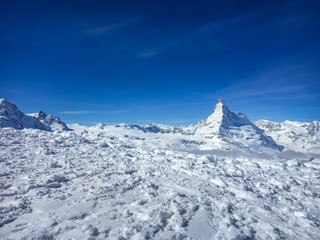 Majestic Matterhorn mountain in front of a blue sky with snow in the foreground.