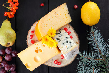 Assortment of cheeses and fruits on dark boards and Christmas tree branches. Swiss cheese, dorblu, Dutch cheese for Christmas. Dairy products, lemon, grapes, pears, pomegranate, rowan berries