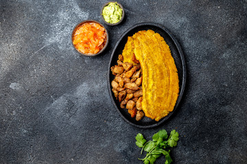COLOMBIAN CARIBBEAN CENTRAL AMERICAN FOOD. Patacon or toston, fried and flattened whole green plantain banana on white plate with tomato sauce and chicharron Black background, top view