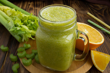 Smoothies with orange and celery on the brown wooden background