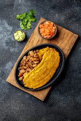 COLOMBIAN CARIBBEAN CENTRAL AMERICAN FOOD. Patacon or toston, fried and flattened whole green plantain banana on white plate with tomato sauce and chicharron Black background, top view