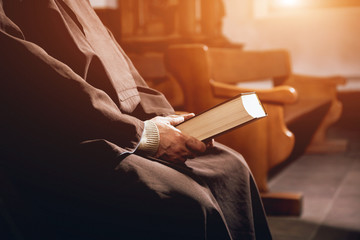 A monk in robes with holy bible in their hands praying in the church - obrazy, fototapety, plakaty