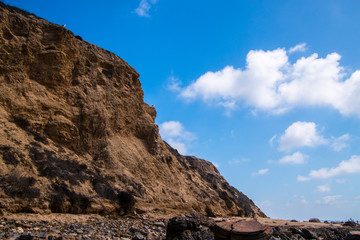 Rugged jagged brown cliff edge with two seagulls. Deep blue sky background with broken puffy clouds