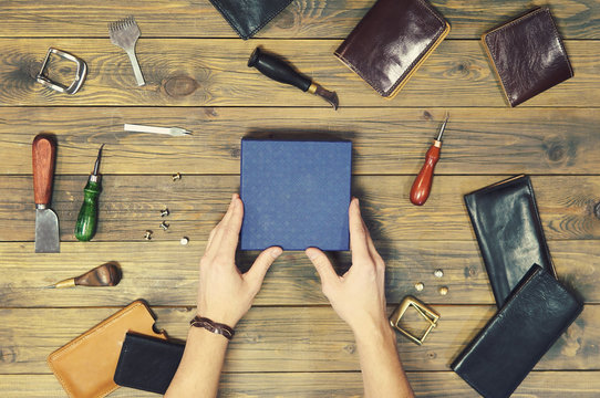 hands put a new leather wallet in a gift box. conceptual image of a gift to a man. composition of different hand made leather man accessories on wooden background