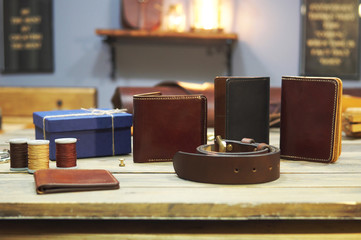 composition of different hand made leather man accessories on wooden background. Wallet, belt, purse, gift box, thread on wooden table