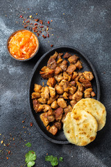 COLOMBIAN FOOD. Fried pork CHICHARRON, AREPAS and colombian tomato sauce. Top view. Black background
