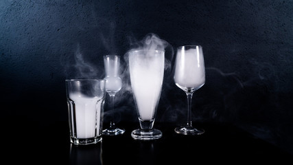 glasses filled with smoke, some glasses on a black table with a black background and some smoke