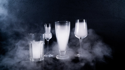 glasses filled with smoke, some glasses on a black table with a black background and some smoke