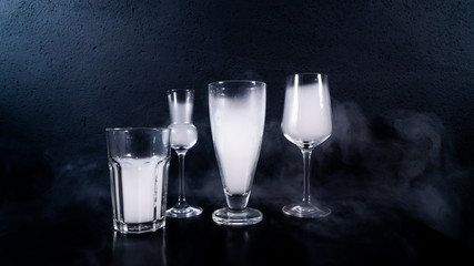 glasses filled with smoke, some glasses on a black table with a black background and some smoke