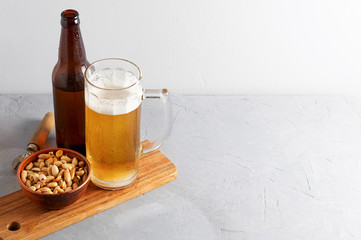 Lager beer pouring in glass and bottle with salted peanuts on gray concrete background