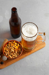 Lager beer pouring in glass and bottle with salted peanuts on gray concrete background