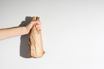 Hand holding beer bottle in the paper bag on gray concrete background