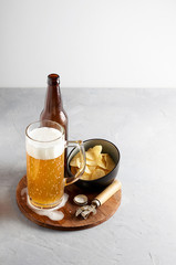 Lager beer in glass and bottle with potato chips on gray concrete background