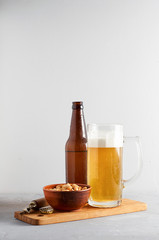 Lager beer pouring in glass and bottle with salted peanuts on gray concrete background