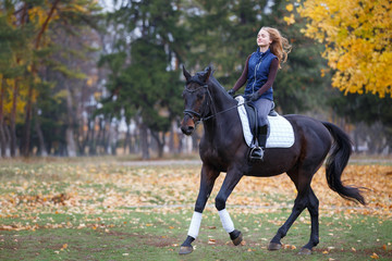 Young rider girl galloping on bay stallion in park