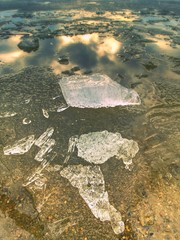 Ice fragments on empty sandy coast. Frozen sand on river coast.