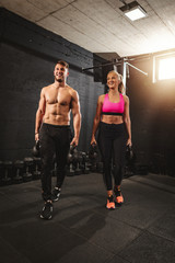 Fototapeta na wymiar Young muscular couple are ready to do hard exercise with kettlebells on cross training at the gym.