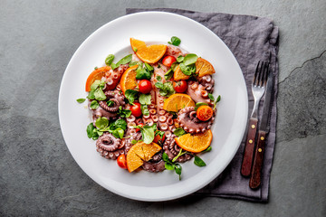 Whole octopus salad with orange, tomatoes and cress salad on white plate. Top view