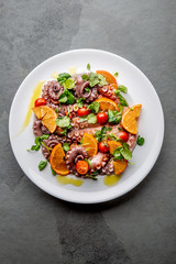 Whole octopus salad with orange, tomatoes and cress salad on white plate. Top view