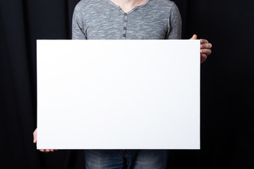 A man holds in his hands a white rectangular blank canvas