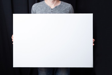 A man holds in his hands a big white rectangular blank canvas