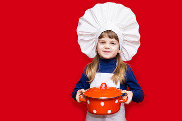 Happy little girl in chef uniform holds saucepan isolated on red. Kid chef. Cooking Concept